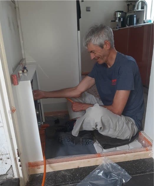 Michel maakt zittend de aansluiting van de vloerverwarming op de verdeler klaar