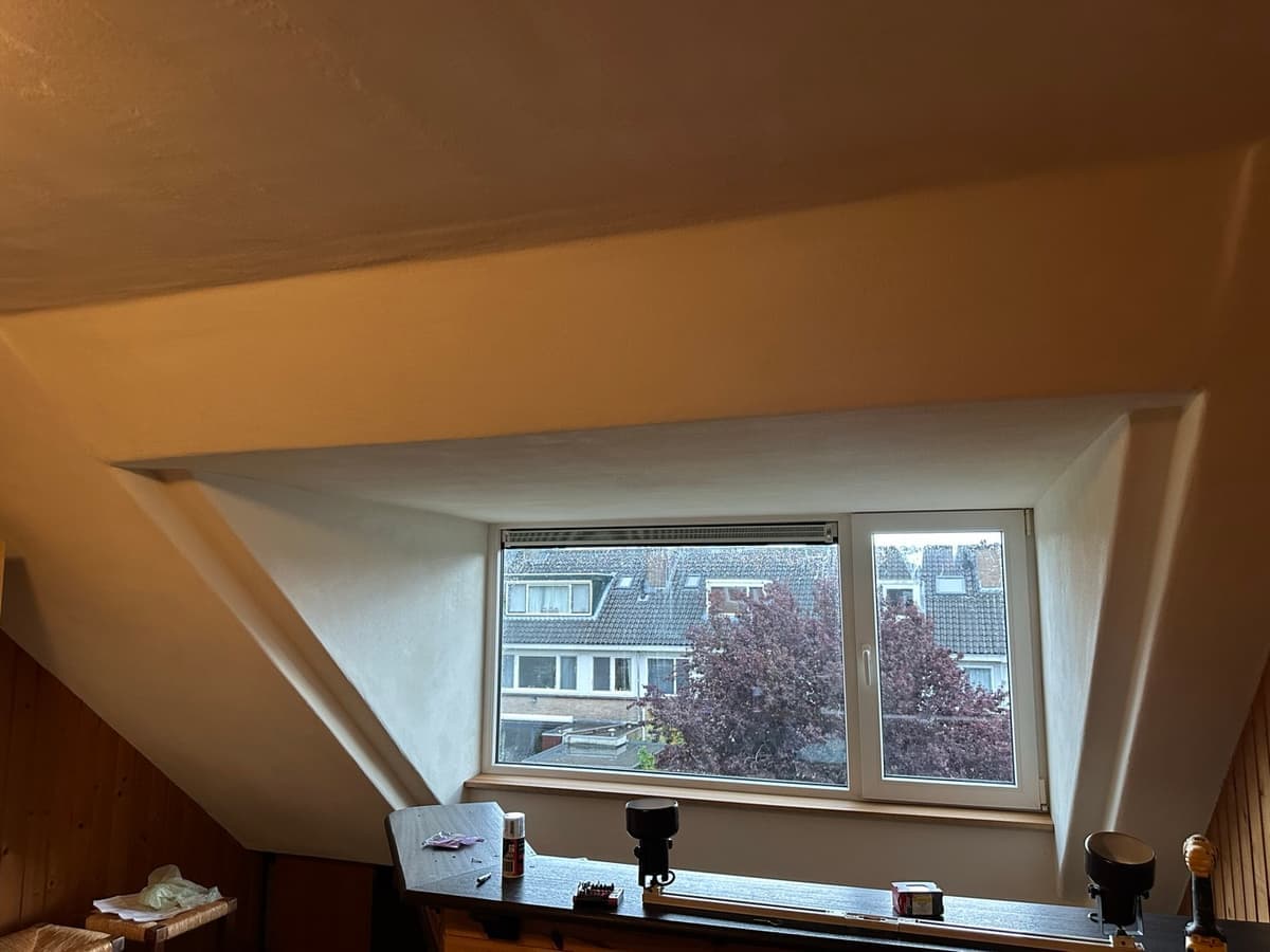 Binnenkant van een dakkapel, strak gestuct, met het schuine dakvlak erboven en uitzicht over de straat